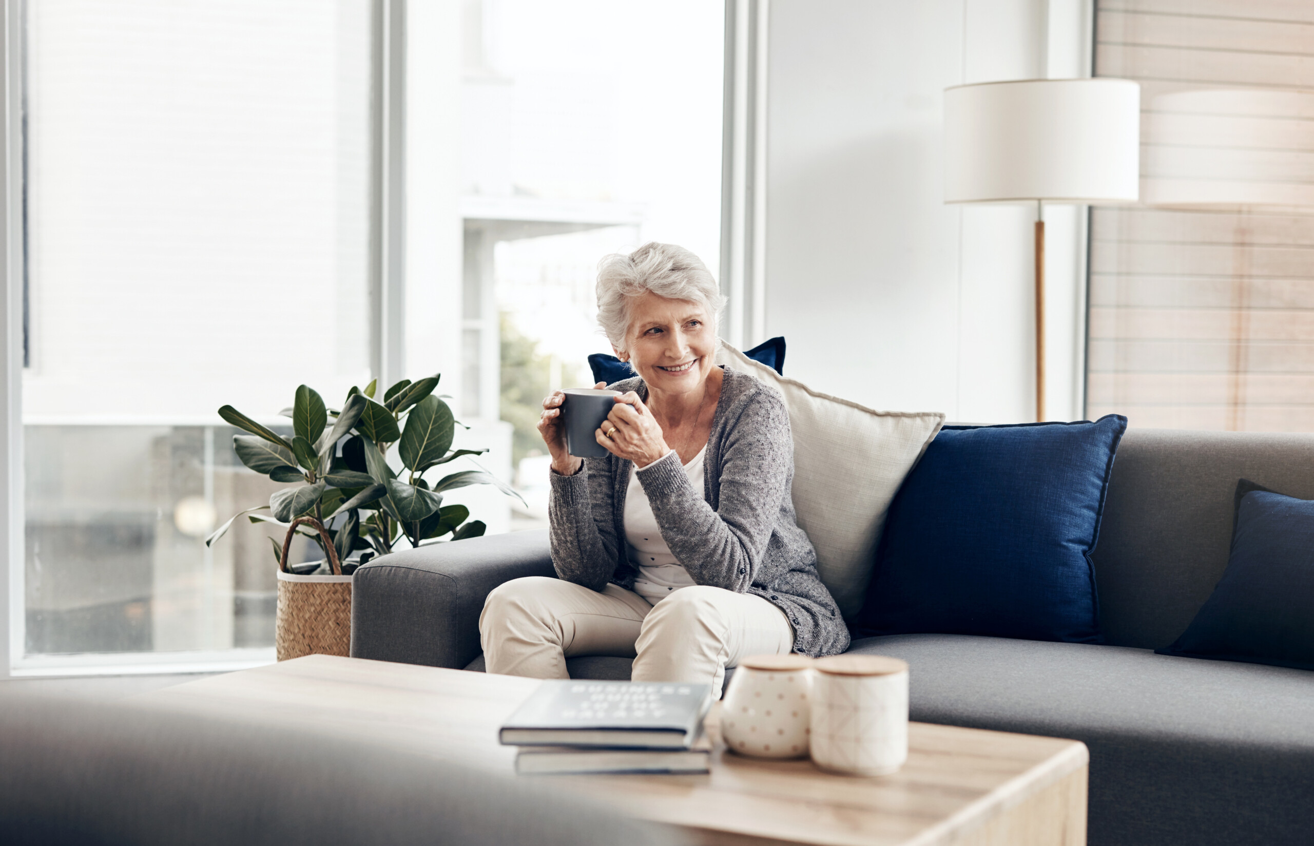 Thinking, coffee and senior woman on sofa with cup for remember, memory or morning routine in living room. Relax, smile and elderly person in thought with herbal tea, caffeine or hot beverage in home.